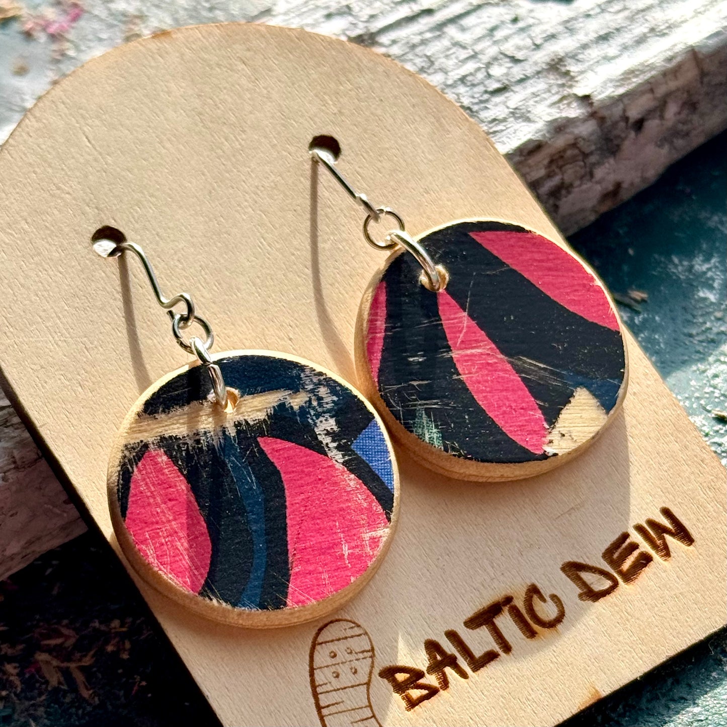 Close view of pink and black skateboard wood drop earrings with petal shapes from the deck graphic