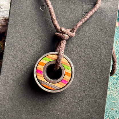 Skateboard bearing pendant with orange, pink and green recycled maple layers on a brown waxed cord.