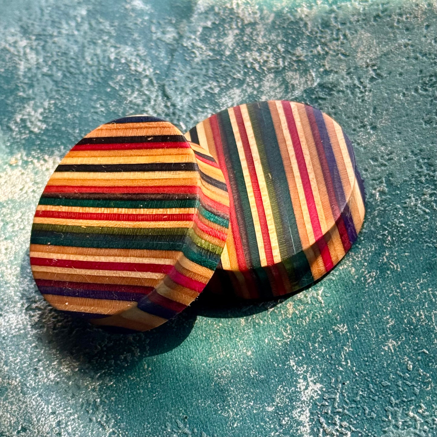 A pair of ear plugs in red, yellow and black skateboard maple, stripes running across the face.