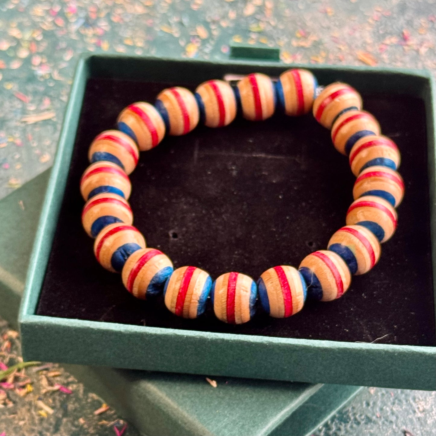 Blue and red beaded bracelet made from recycled skateboard maple, shown from above in its box
