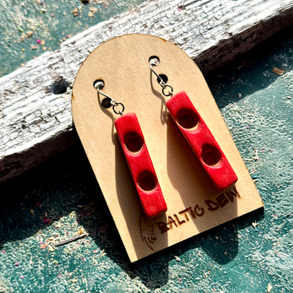 Red recycled skateboard wood bar earrings with carved round hollows, resting on weathered wood