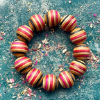 Chunky red, pink, black and teal skateboard maple bead bracelet in a full round among wood shavings.