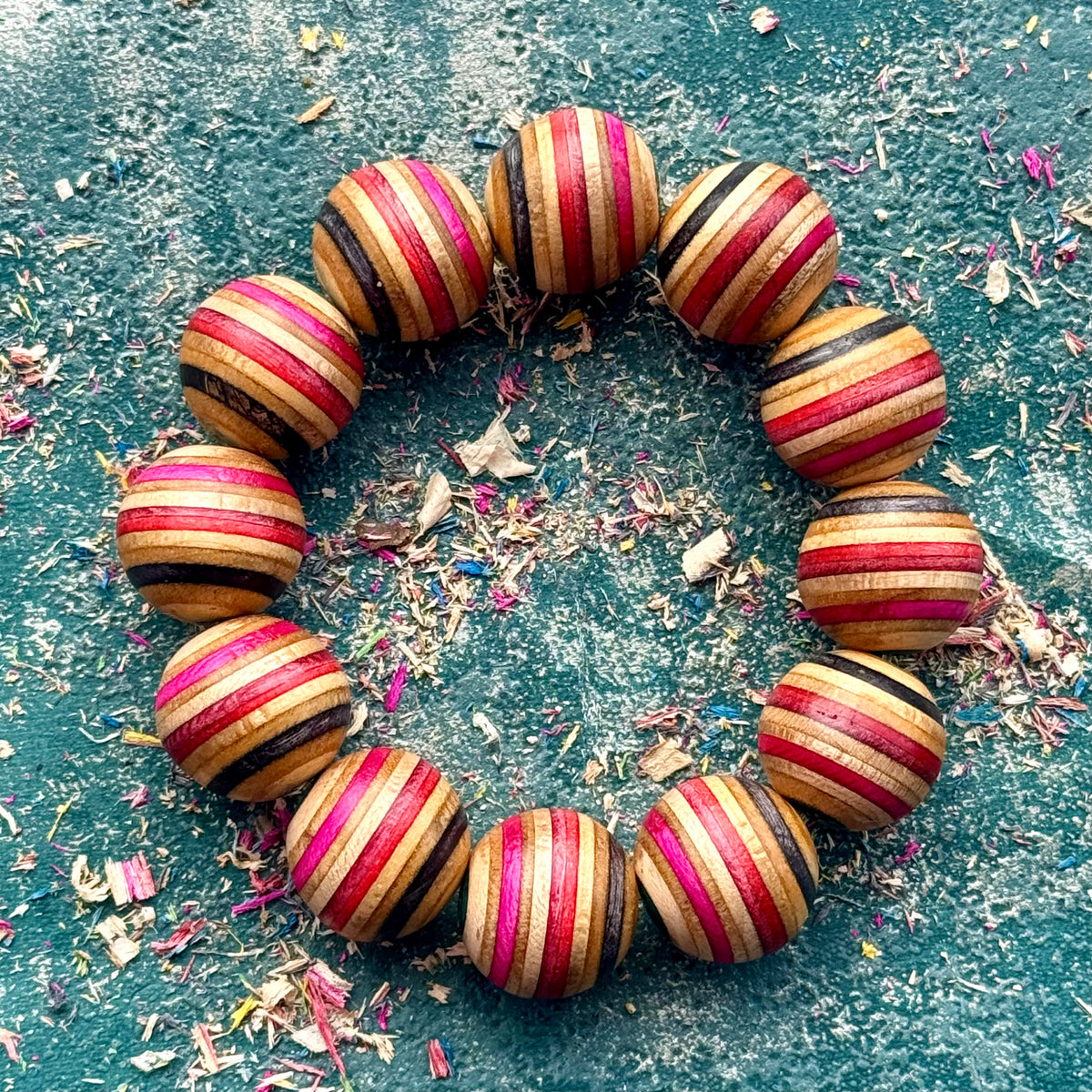Chunky red, pink, black and teal skateboard maple bead bracelet in a full round among wood shavings.
