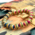 Pink and green recycled skateboard wood bead bracelet on a broken deck, the maple layers striping every bead.