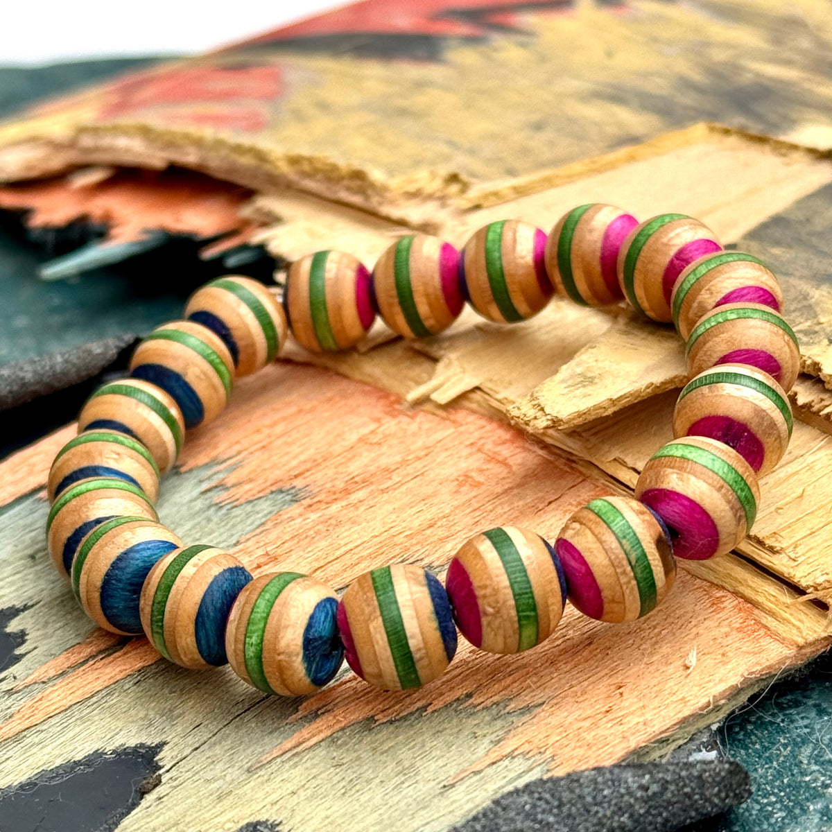 Pink and green recycled skateboard wood bead bracelet on a broken deck, the maple layers striping every bead.