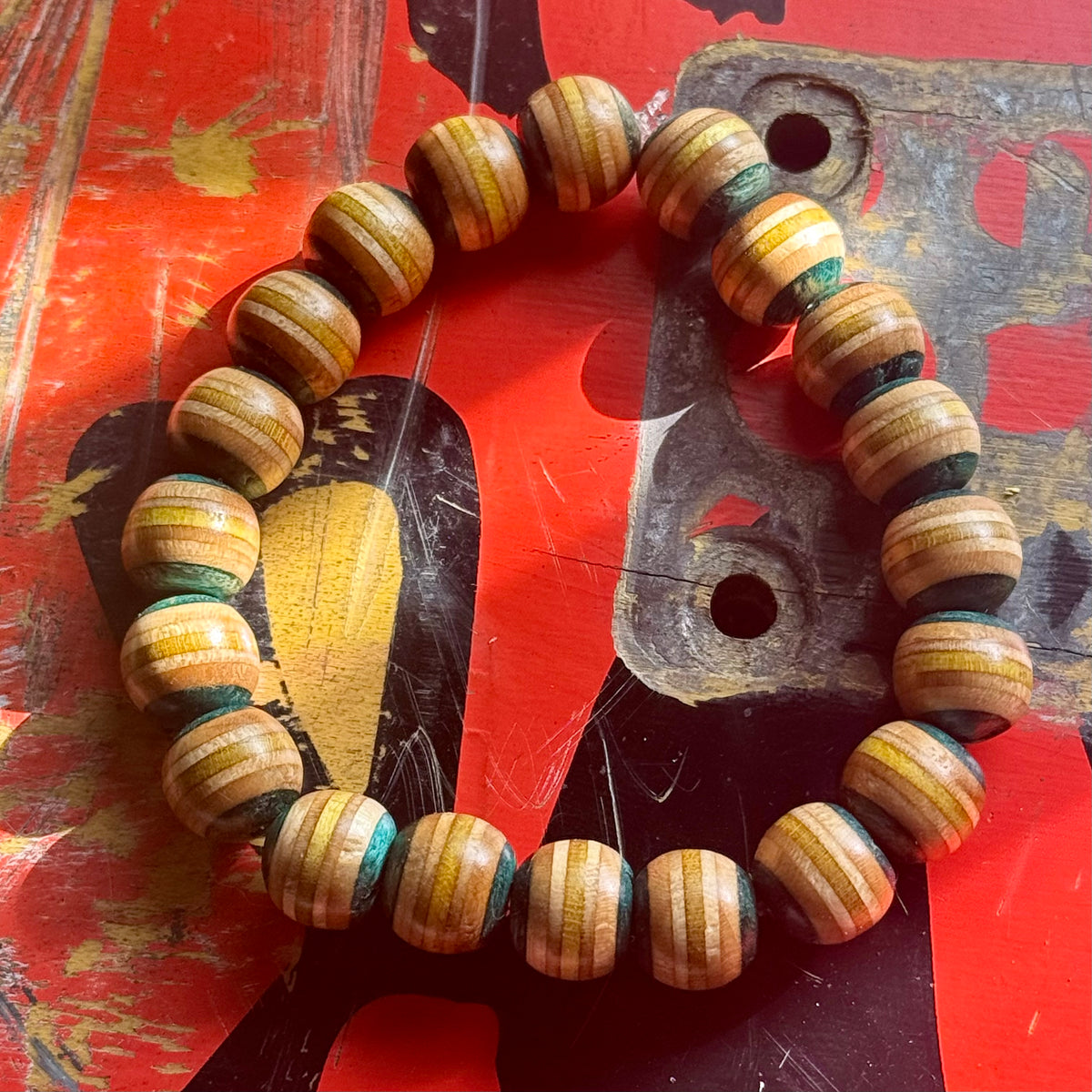 Light teal and yellow recycled skateboard bracelet on a red deck with an old truck baseplate, handmade by Baltic Dew.