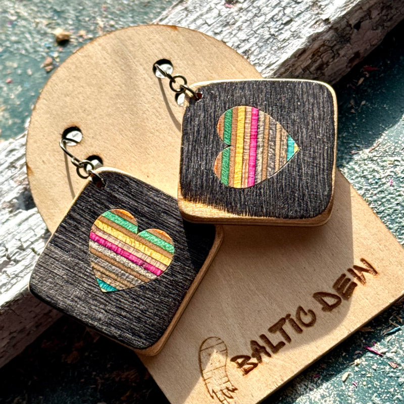 Black recycled skateboard square drop earrings with heart cut-outs, showing pink, yellow and blue layered maple.