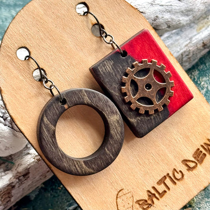 Close view of a charcoal wooden ring and red square earring with a decorative brass cog