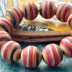Close-up of chunky recycled skateboard wood beads with red, pink, black and teal layers, handmade by Baltic Dew.