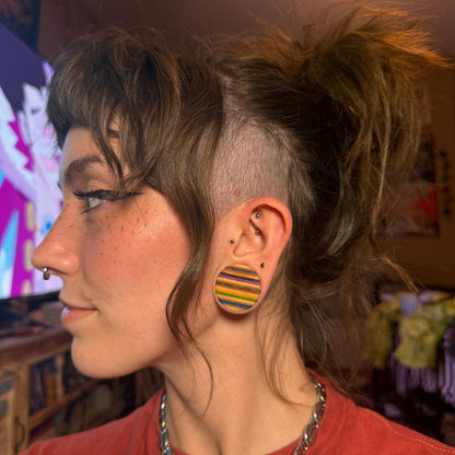 Wooden ear plug worn in a stretched lobe, side profile showing the coloured stripes.