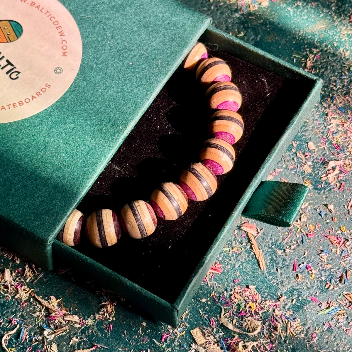 Brown, black and purple recycled skateboard wood bead bracelet in its green Baltic Dew gift box.