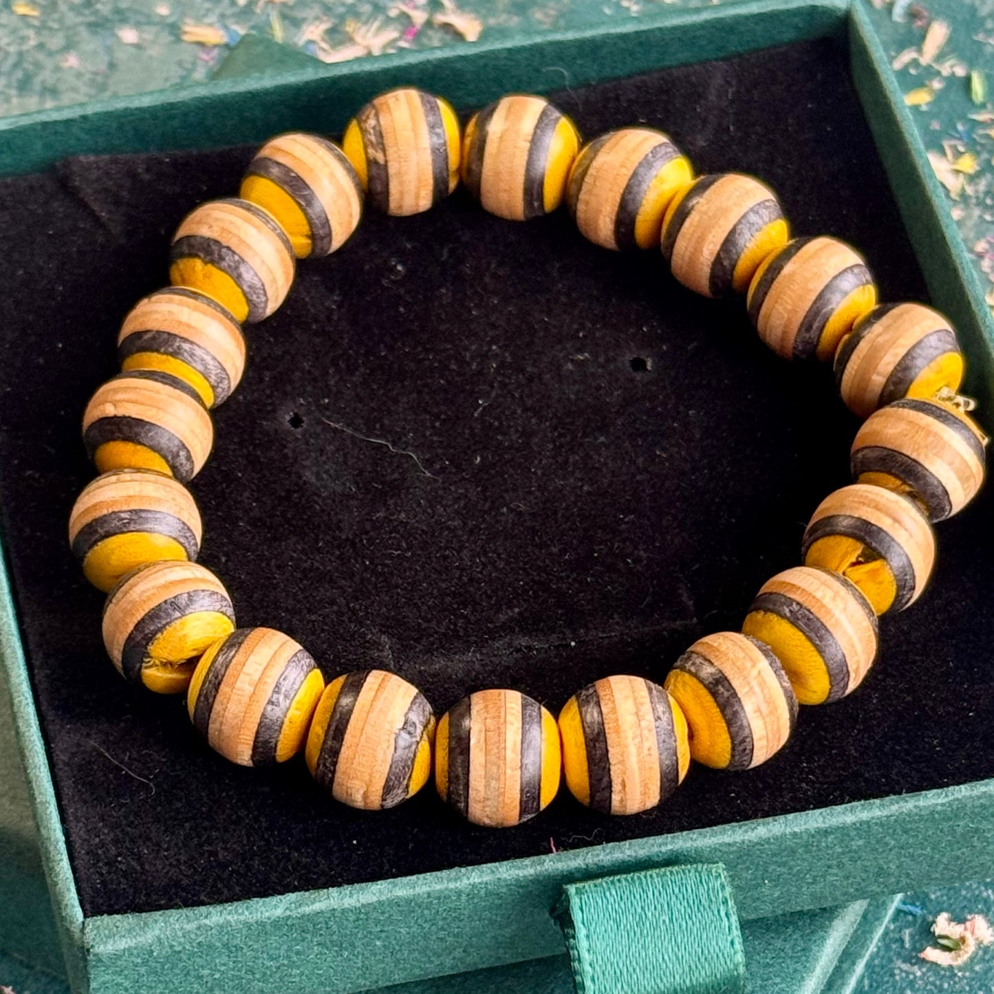 Yellow and black beaded bracelet made from recycled skateboard maple, shown from above in its box