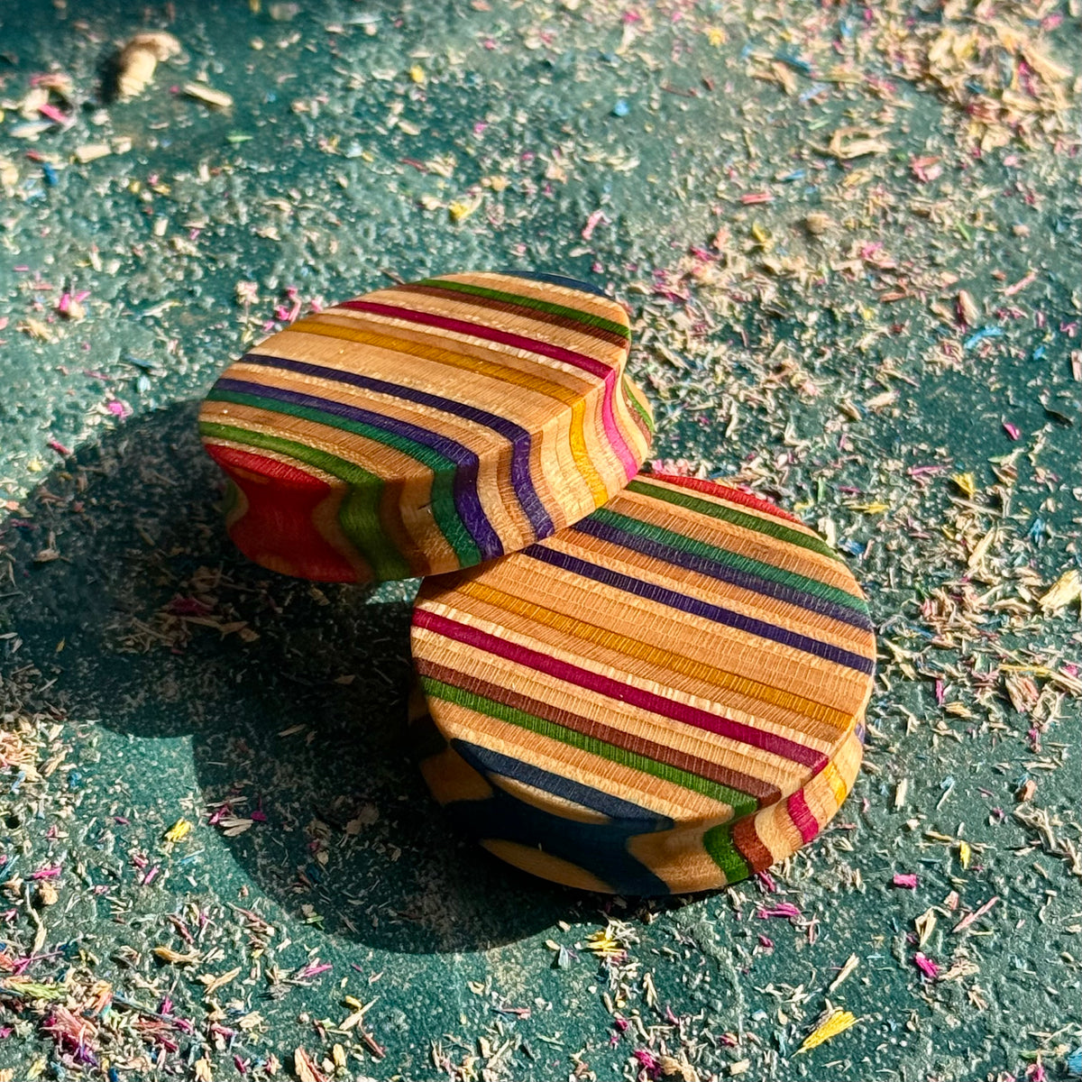 Two round plugs with fine red, purple and green stripes across the skateboard maple face.