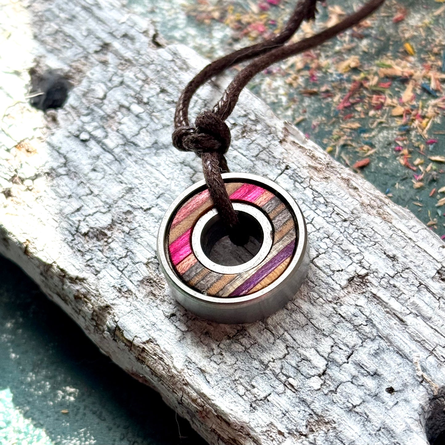 Skateboard bearing pendant necklace with pink, grey and natural maple layers on a brown waxed cotton cord.