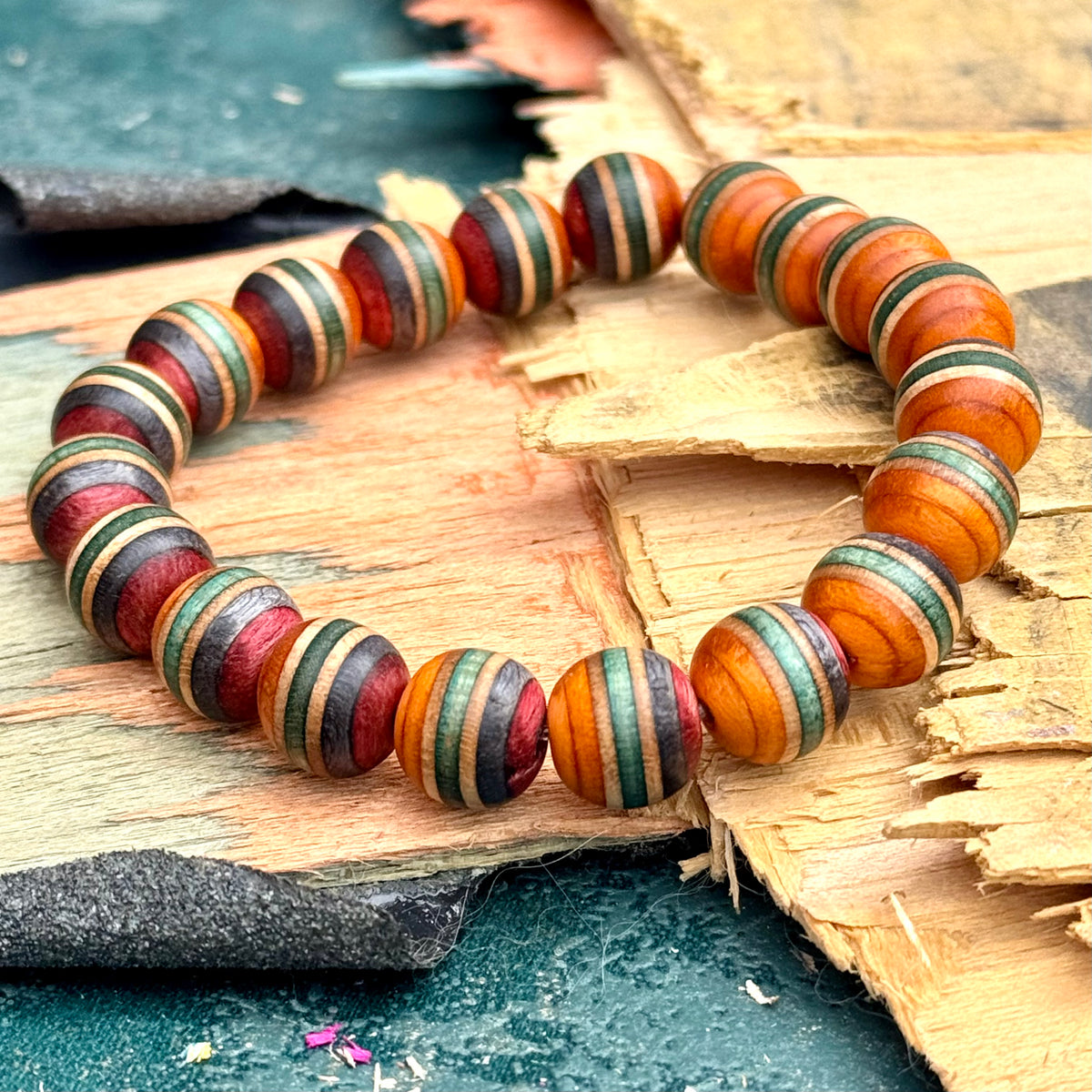 Close view of striped orange and red skateboard maple beads with green and pale maple bands, resting on a broken deck.