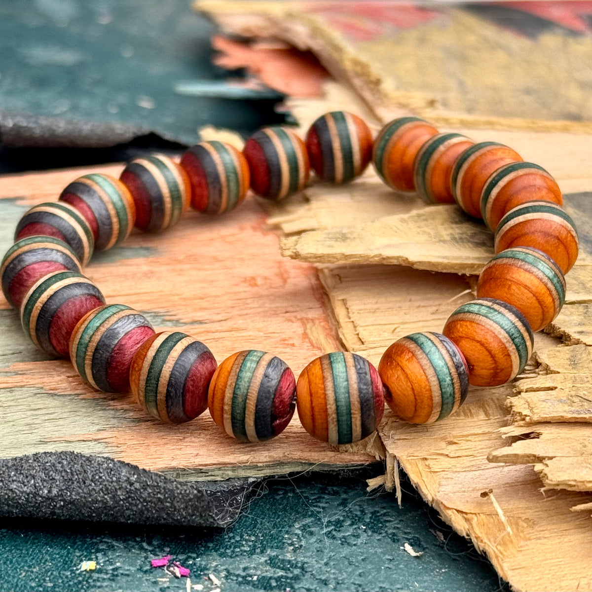 Round wooden bead bracelet in orange, green and red on a broken skateboard deck, the maple layers striping each bead.