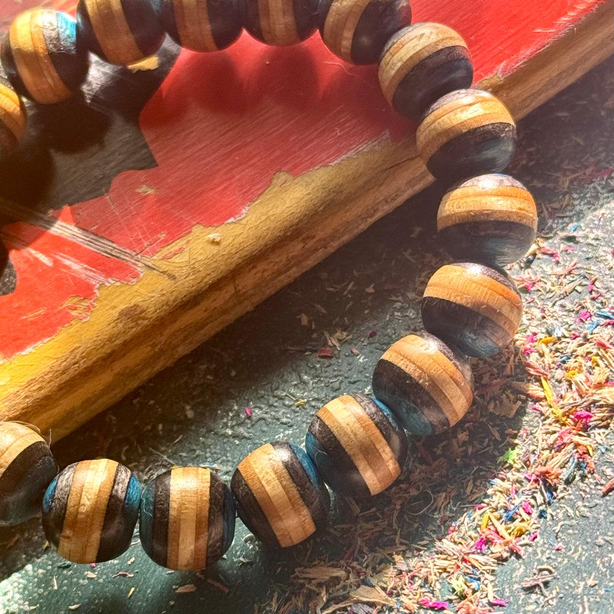 Close-up of blue and black striped beads cut from recycled skateboard maple, resting on a red and yellow deck.