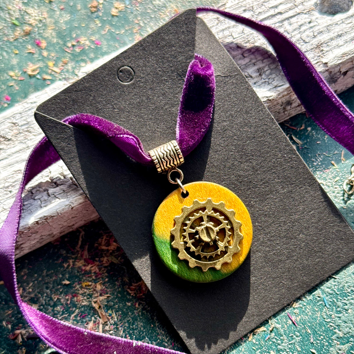 Yellow and green round gear pendant in recycled skateboard maple on a purple velvet choker ribbon.