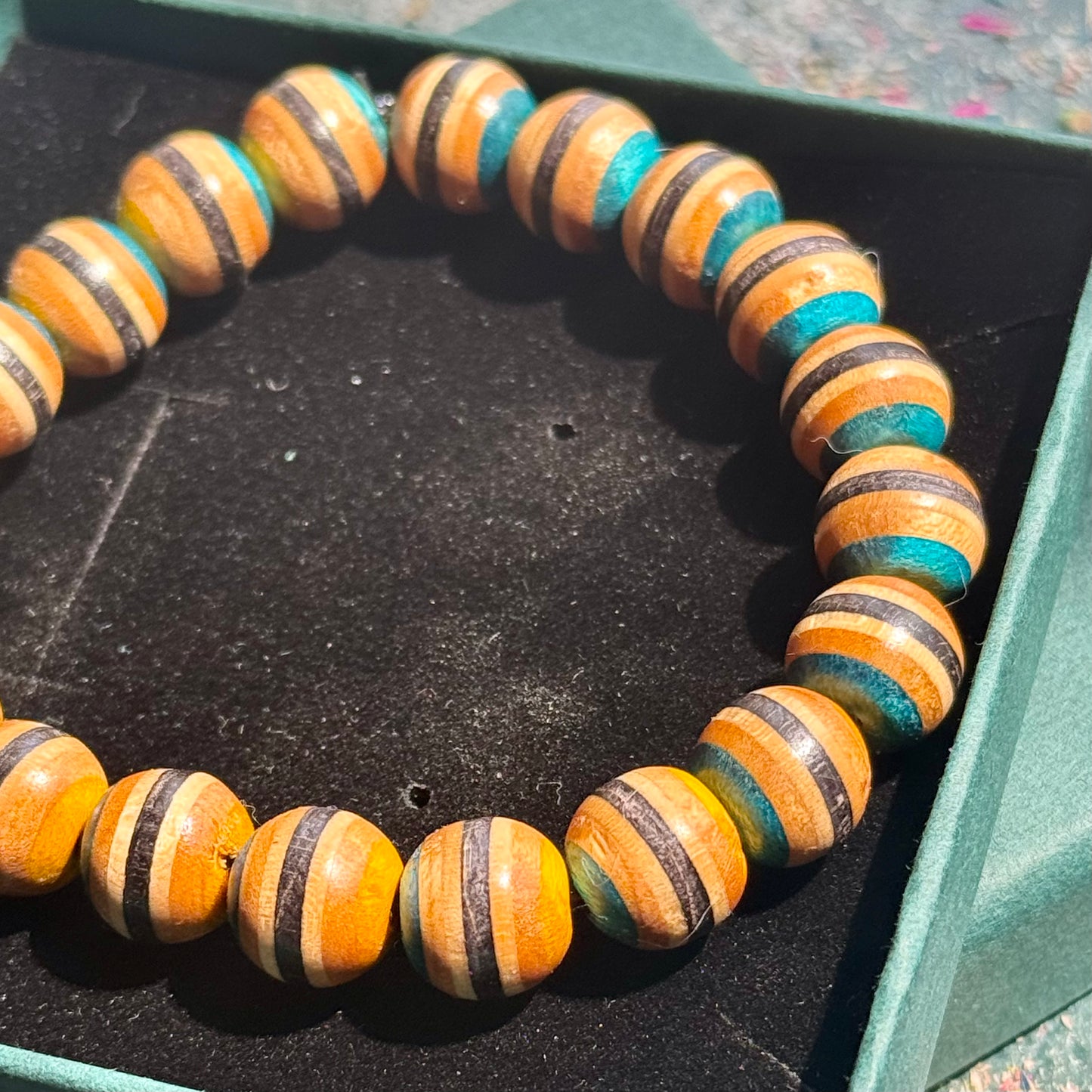 Yellow and Blue Skateboard Bracelet featuring round beads with layered wood and blue accents made from recycled skateboards, displayed in a black box.