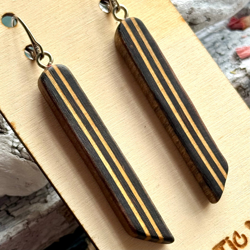 Close view of a black skateboard wood long drop earring showing the cream maple layers as stripes