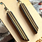 Close view of a black skateboard wood long drop earring showing the cream maple layers as stripes