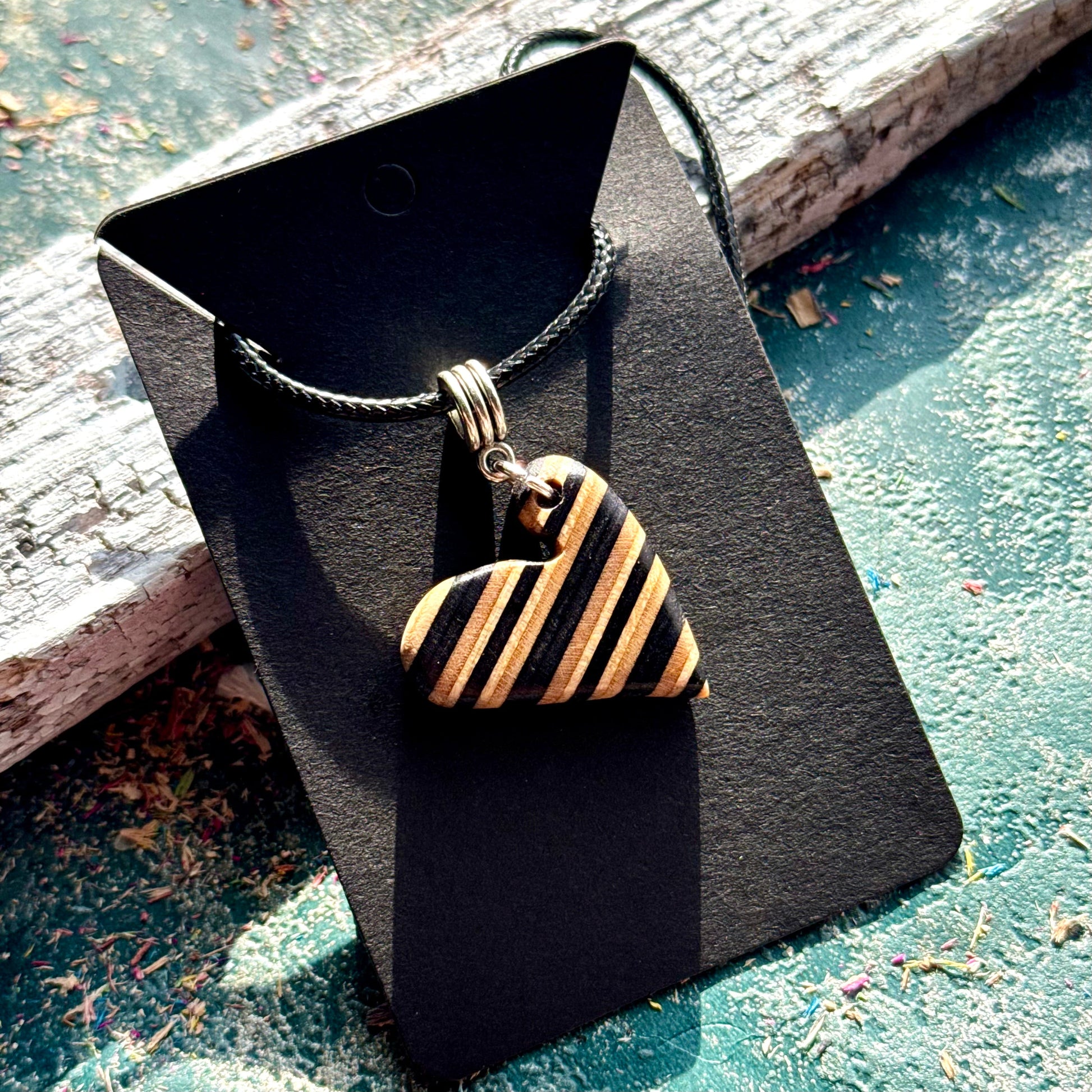Close view of a black and natural maple heart pendant showing the skateboard deck layers as stripes.