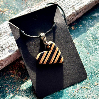 Close view of a black and natural maple heart pendant showing the skateboard deck layers as stripes.