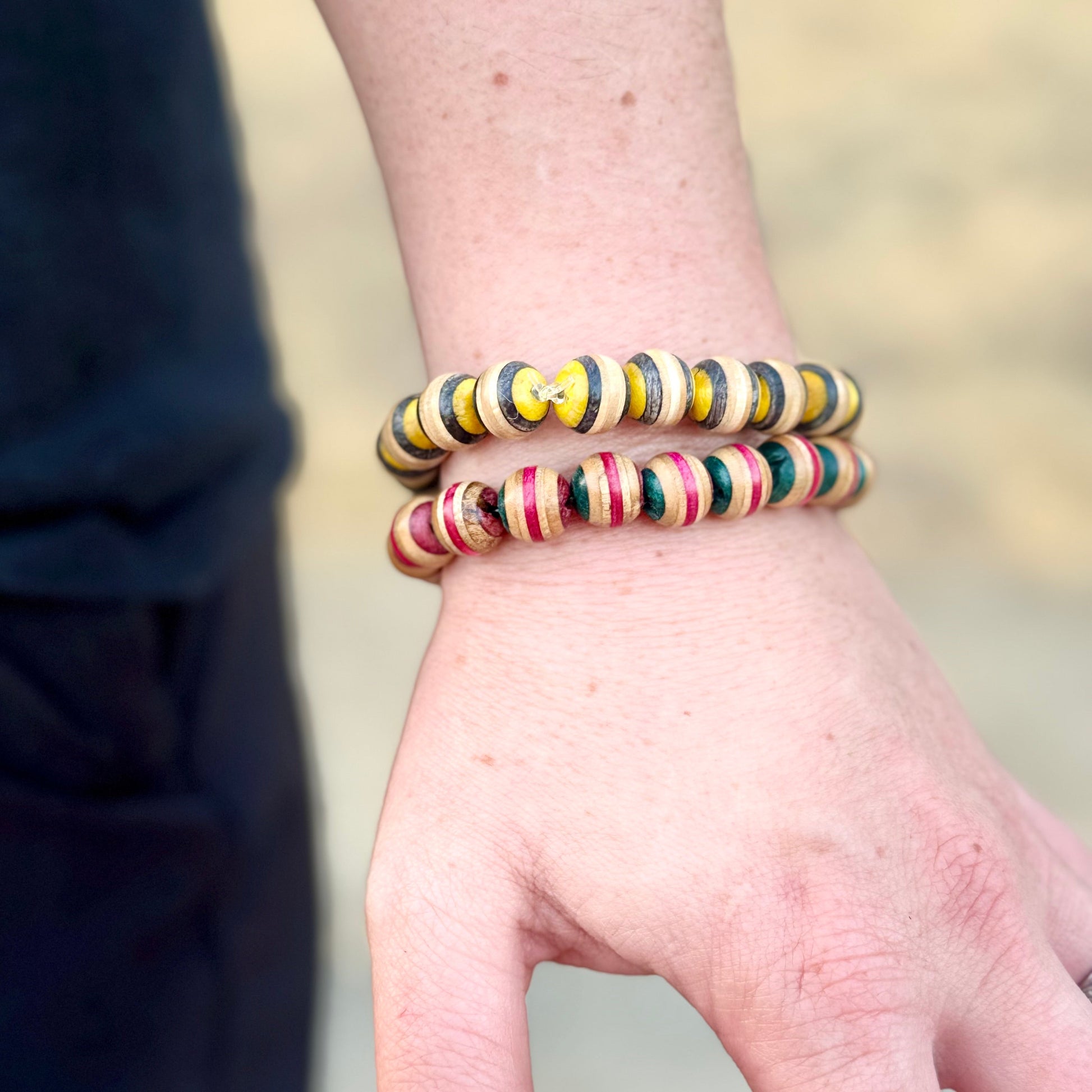 Yellow and black skateboard wood bead bracelet worn on the wrist, stacked with a pink colourway.
