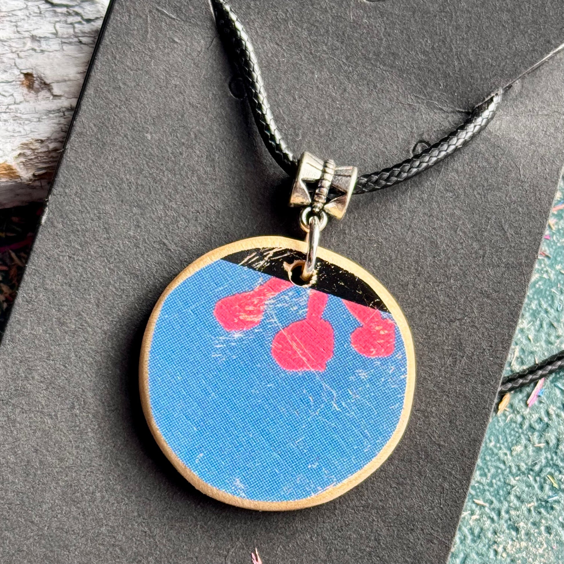 Round blue wooden pendant showing three pink flower stamens from the skateboard deck's graphic.