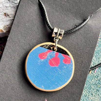Round blue wooden pendant showing three pink flower stamens from the skateboard deck's graphic.