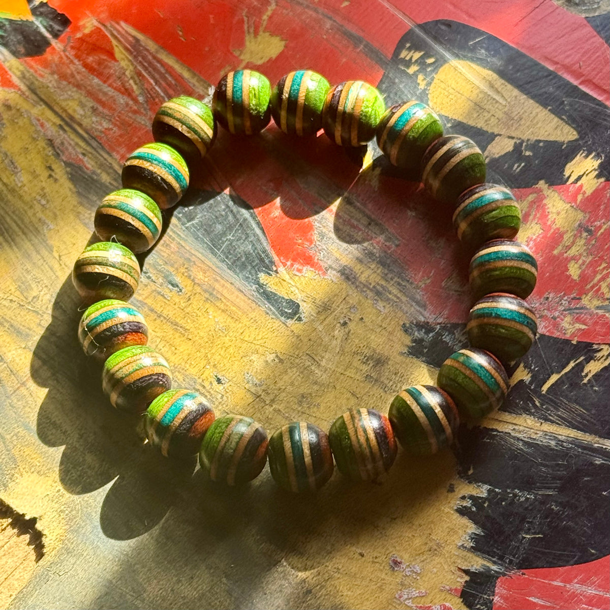 Green, teal and brown striped maple beads from a recycled skateboard deck, strung on elastic cord.