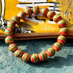 Red, green and teal wood bead bracelet from recycled skateboard maple in a full round on a yellow deck.