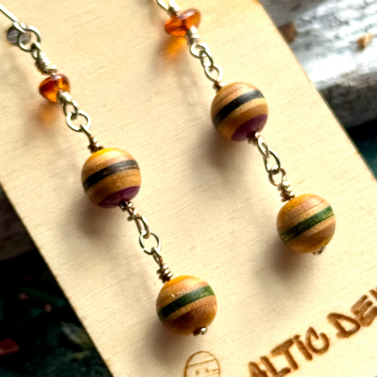 Yellow, purple and green striped skateboard wood beads below a piece of Baltic amber on a drop earring