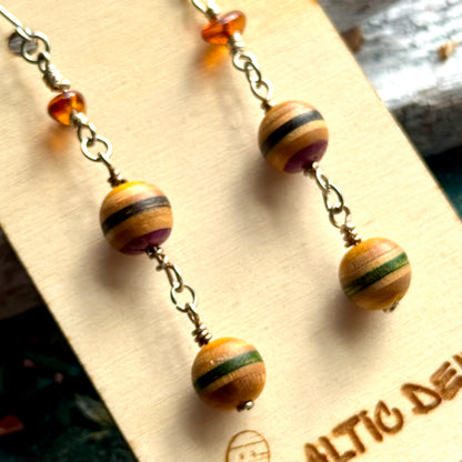 Yellow, purple and green striped skateboard wood beads below a piece of Baltic amber on a drop earring