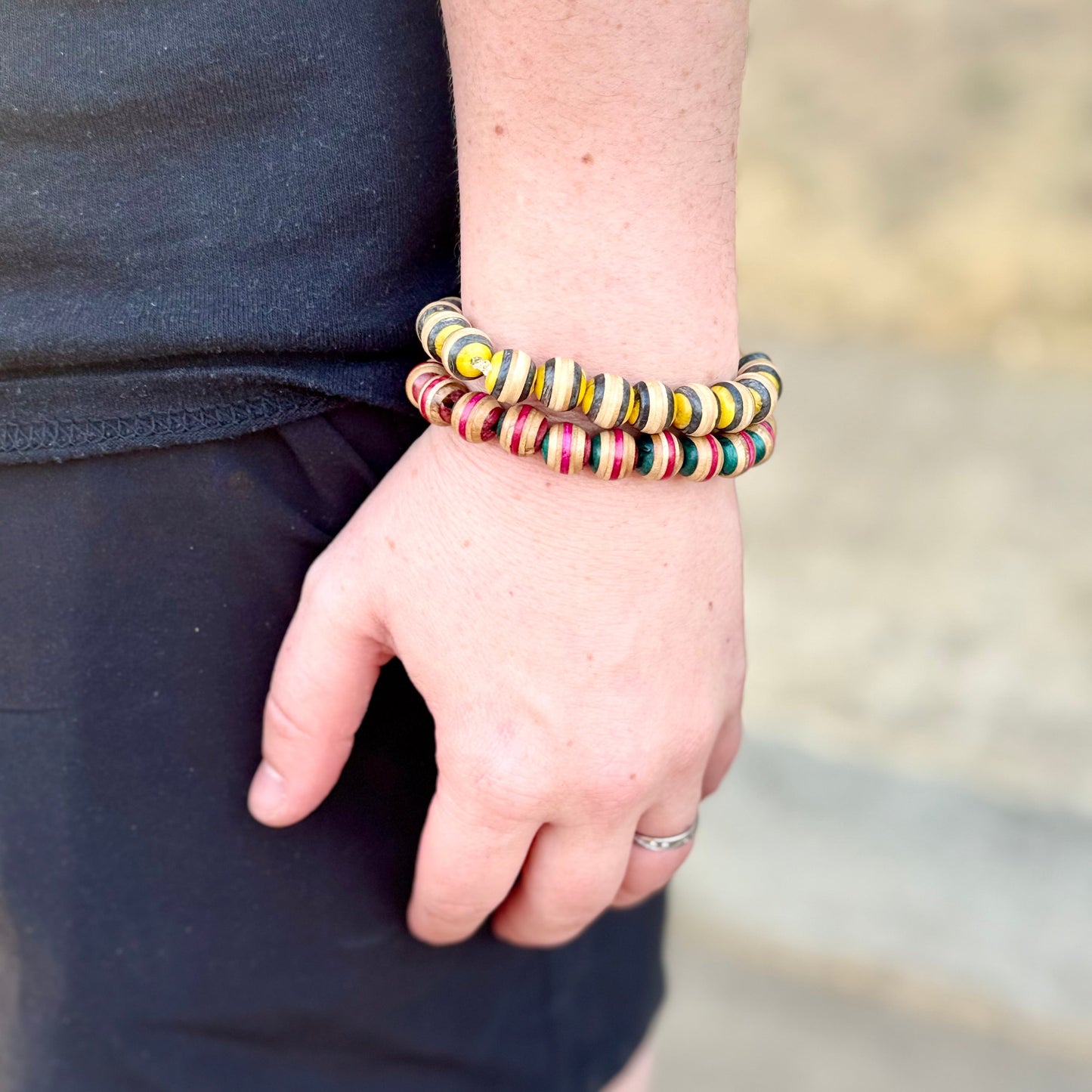 Yellow and black skateboard wood bead bracelet worn stacked on the wrist outdoors, handmade by Baltic Dew.