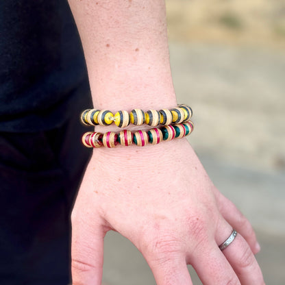 Yellow and black recycled skateboard bead bracelet on the wrist, the black bands clear against the maple.
