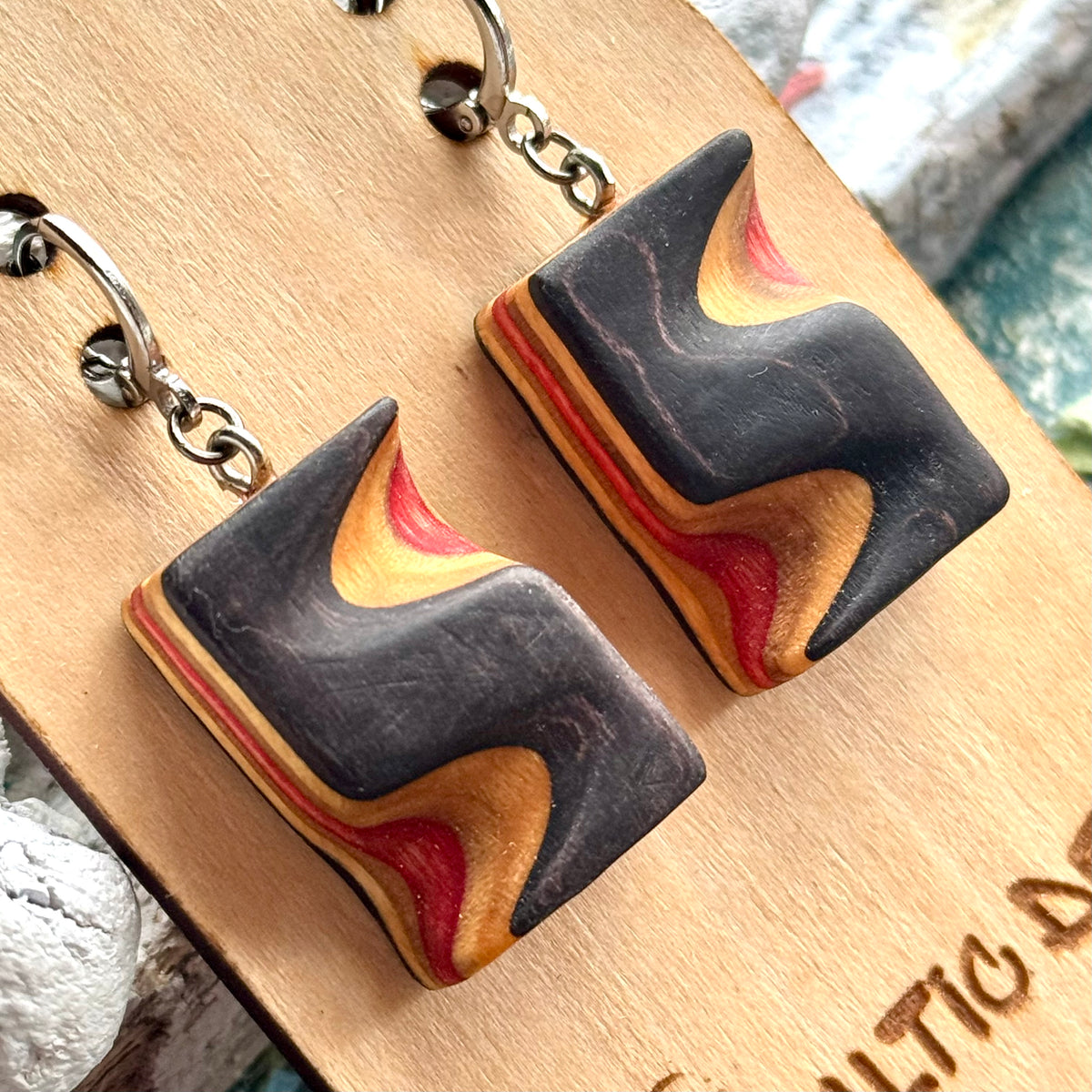 Close view of black and red carved wave earrings cut from a recycled skateboard deck