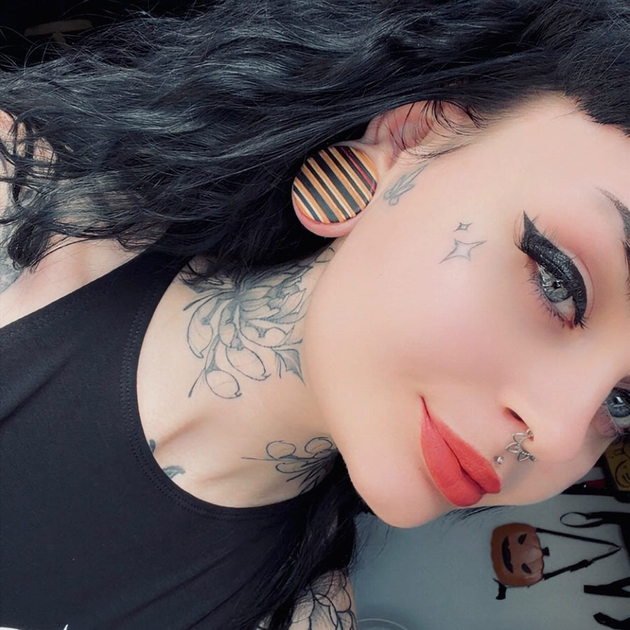 Striped wooden ear plug worn in a stretched ear