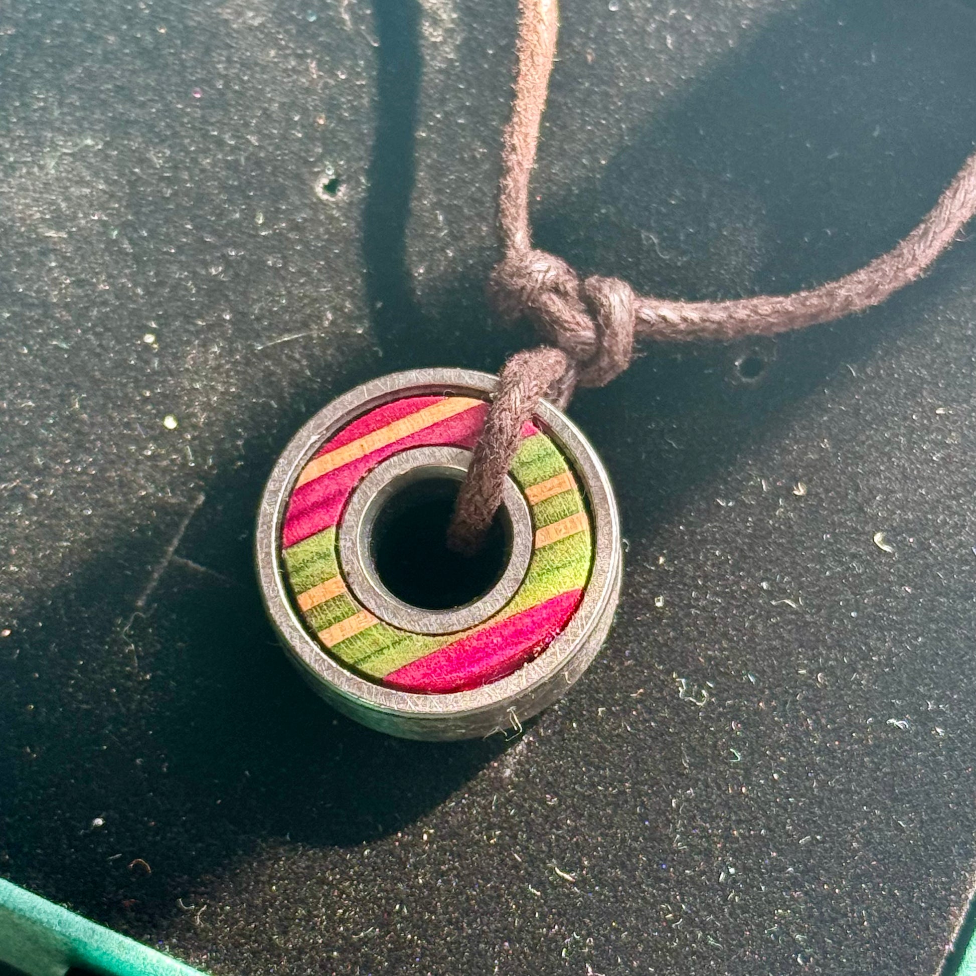 Close-up of a skateboard bearing pendant necklace with pink, green and pink maple colour layers.