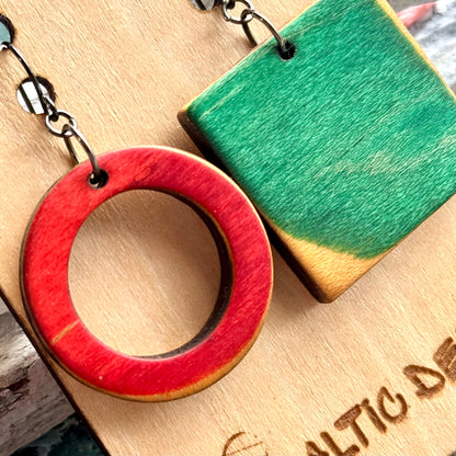 Close view of a red wooden ring and green square earring cut from recycled skateboard maple