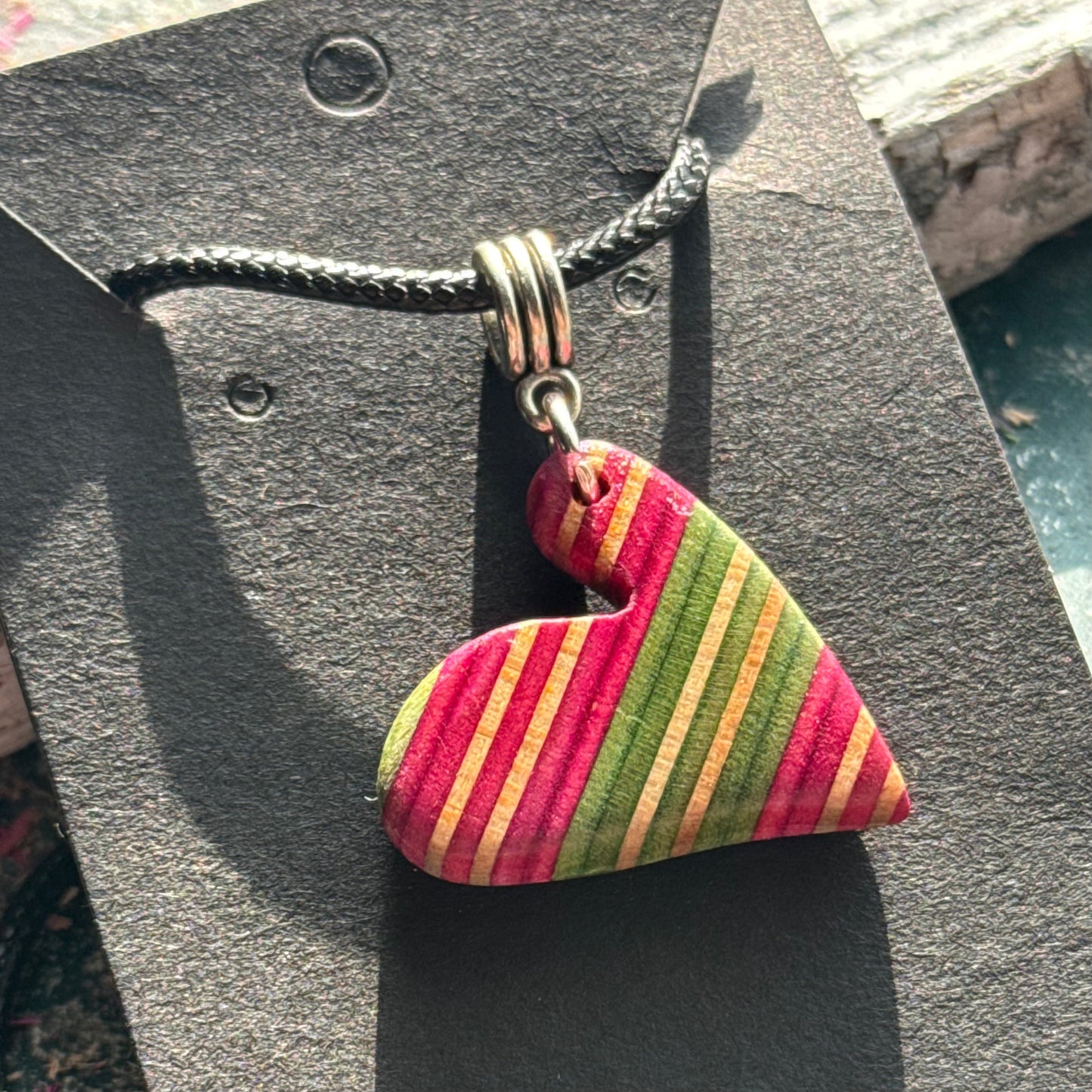 Pink and green striped wooden heart pendant from recycled skateboard maple on a black waxed cord.