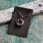 Skateboard bearing pendant necklace with black and natural maple stripes, shown on a Baltic Dew card.