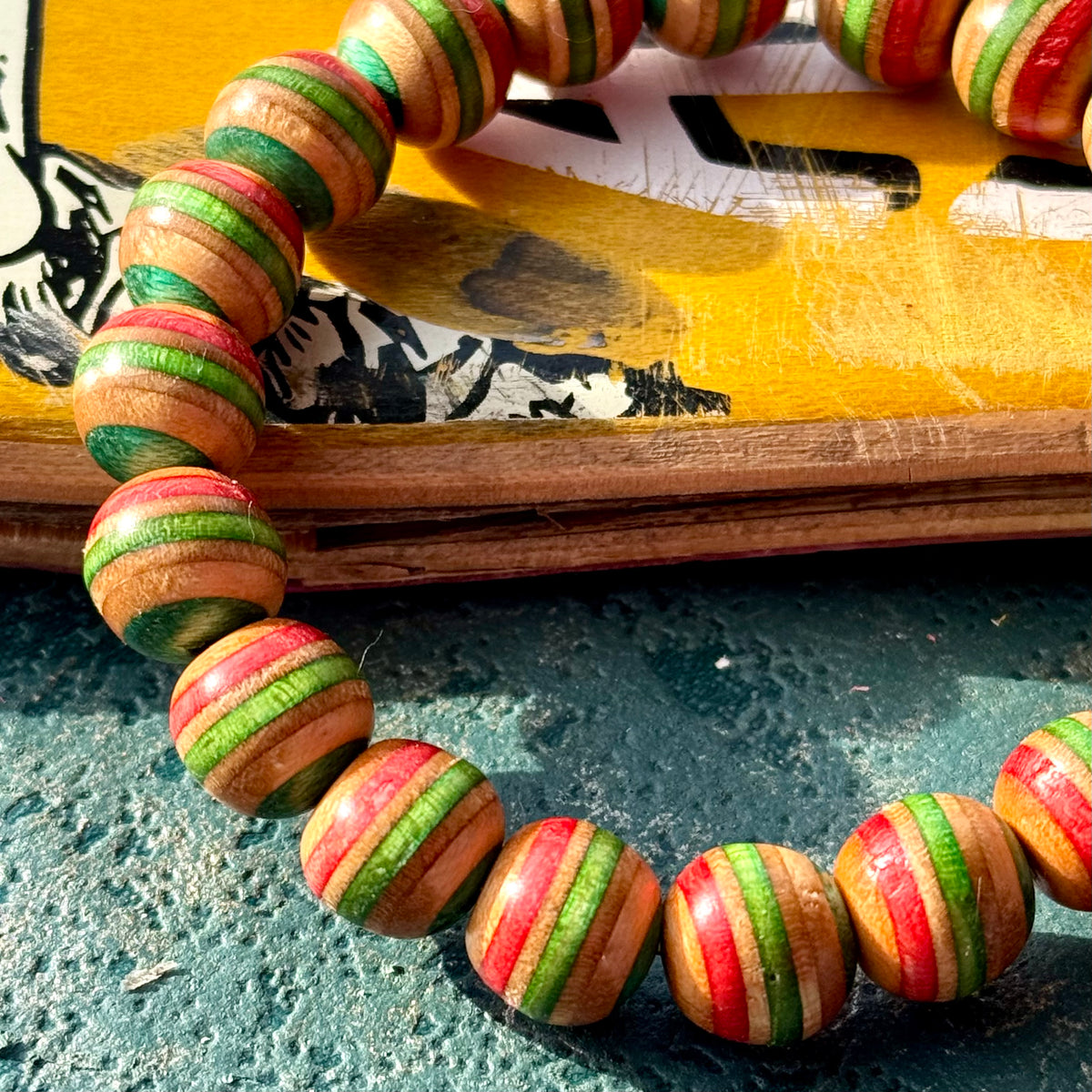 Red, green and teal recycled skateboard bracelet resting against a printed yellow skateboard deck.