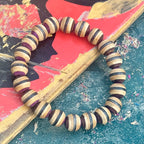 Recycled skateboard bracelet with purple, brown and black striped maple beads, resting across a worn skateboard deck.