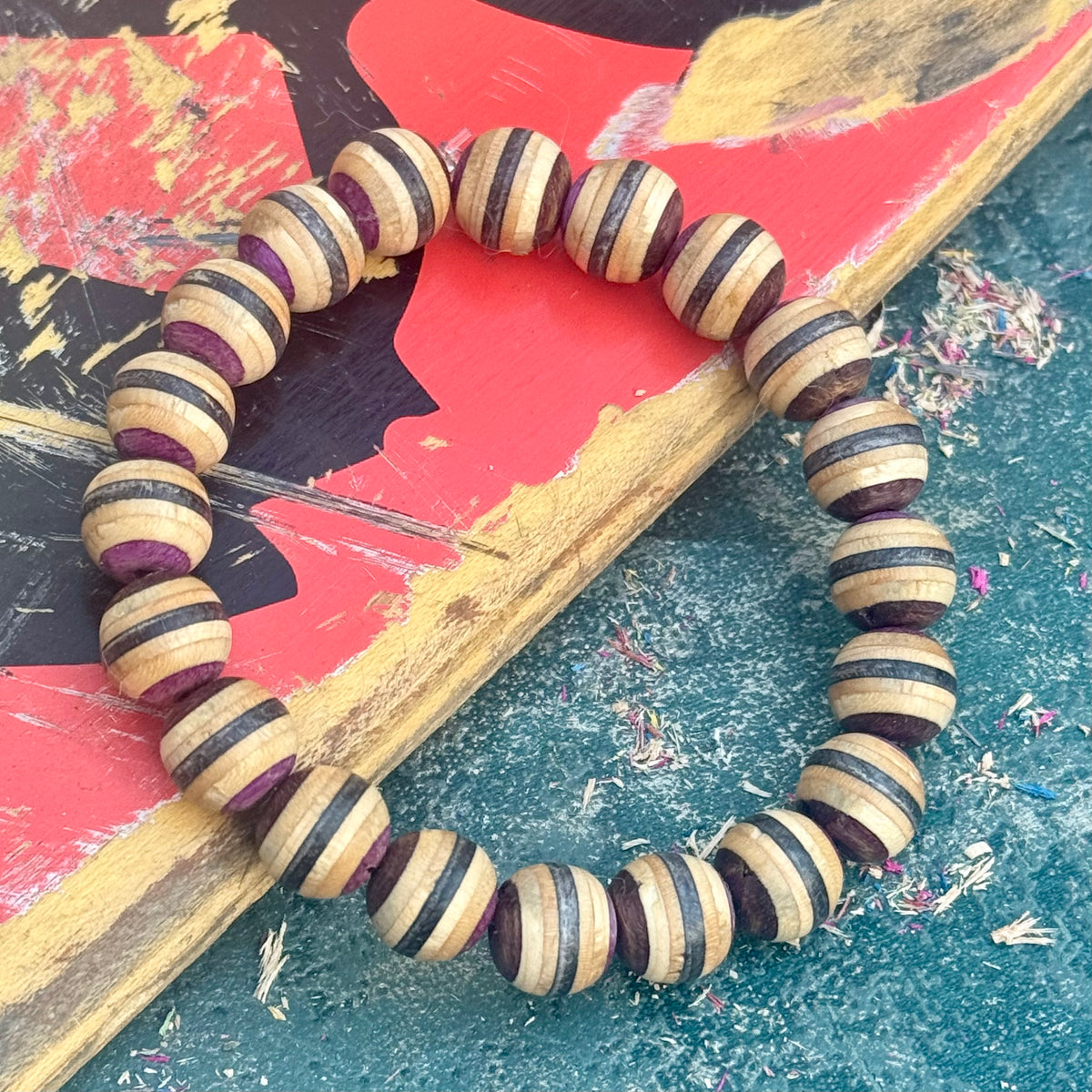 Recycled skateboard bracelet with purple, brown and black striped maple beads, resting across a worn skateboard deck.