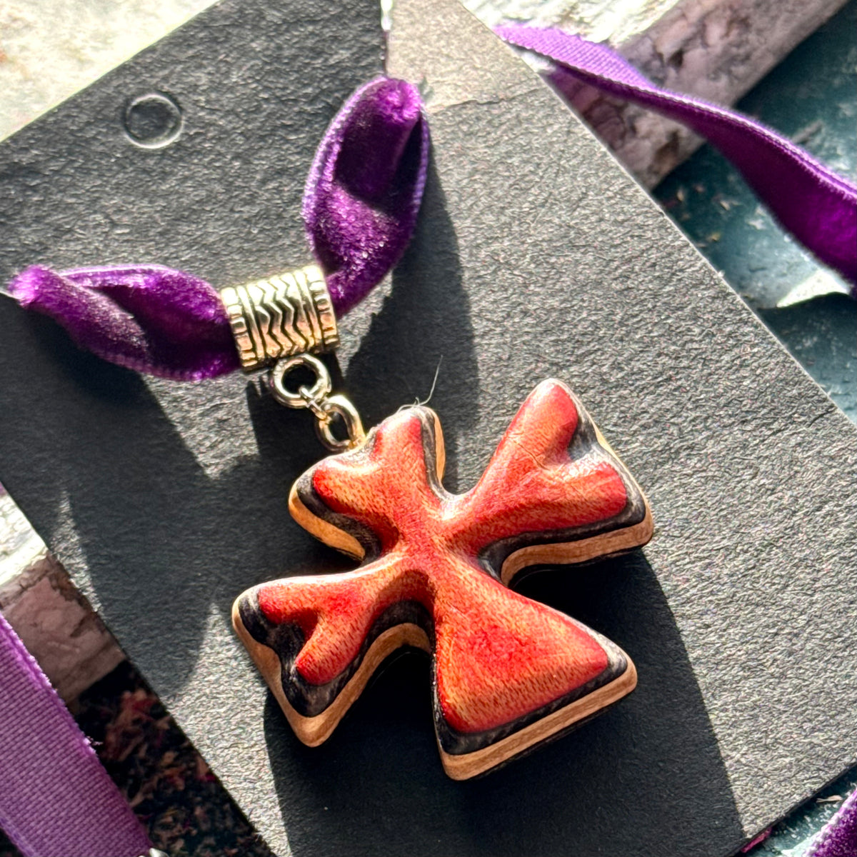 Red clover pendant in recycled skateboard maple with black edge layers on a purple velvet choker.