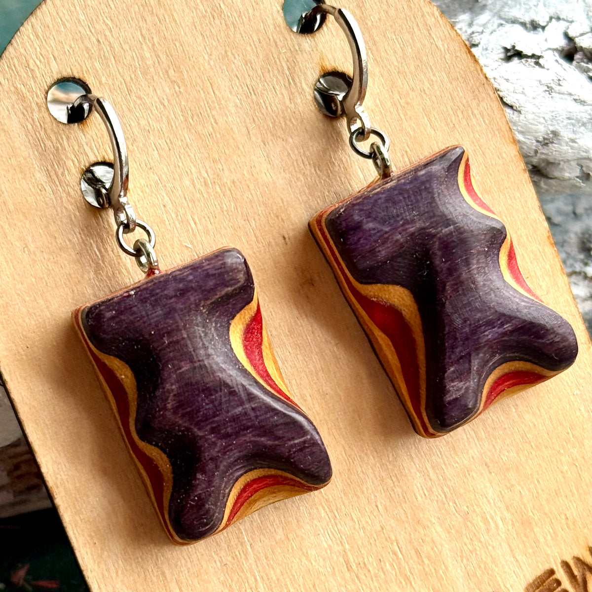 Close view of purple and red carved wave earrings, handmade by Baltic Dew from deck maple