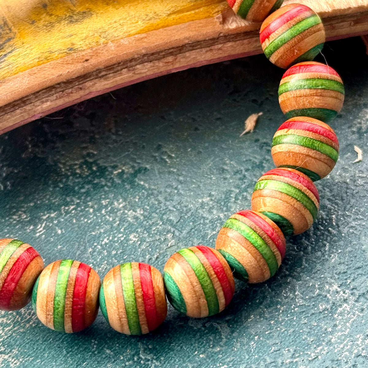 Recycled skateboard bracelet with red, green and teal maple beads beside a split skateboard deck.