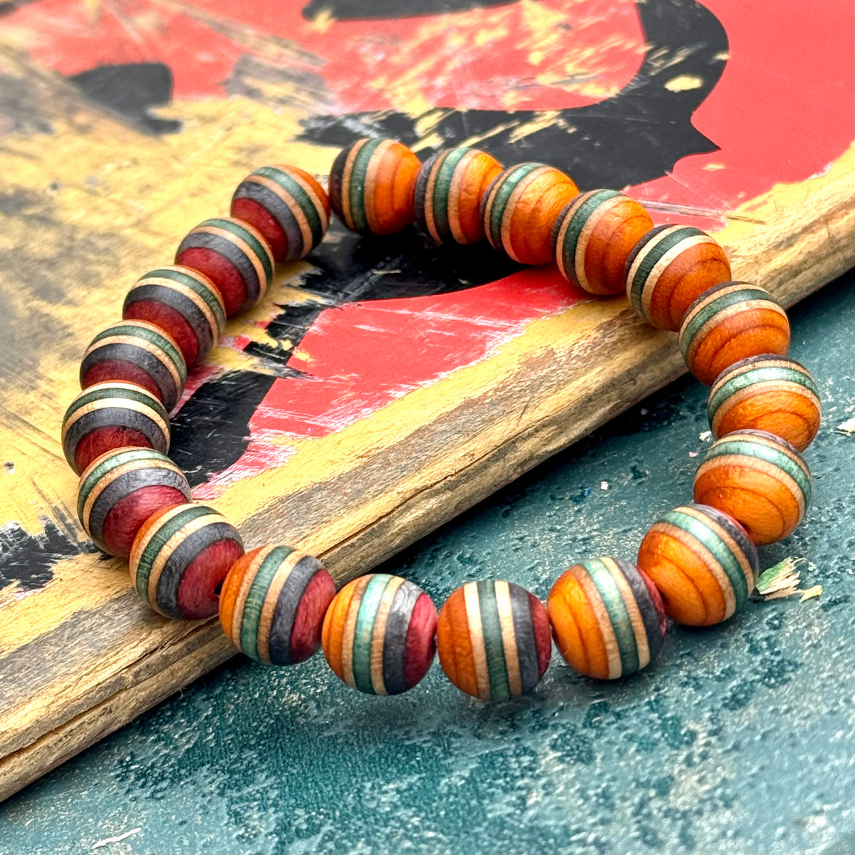 Orange, green and red recycled skateboard wood beads laid over a printed deck graphic, handmade by Baltic Dew.