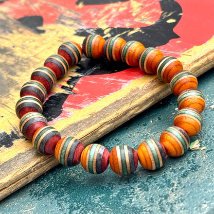 Orange, green and red recycled skateboard wood beads laid over a printed deck graphic, handmade by Baltic Dew.